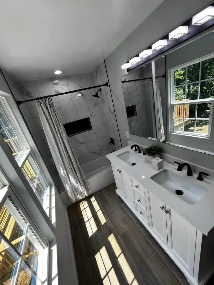 Remodeled bathroom with a double vanity, framed mirrors and a tiled tub and shower surround