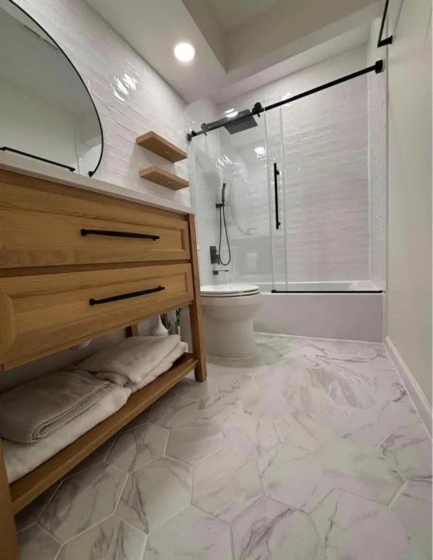 Tub and shower with sliding glass doors, white tile walls and hexagon marble-look floor tile